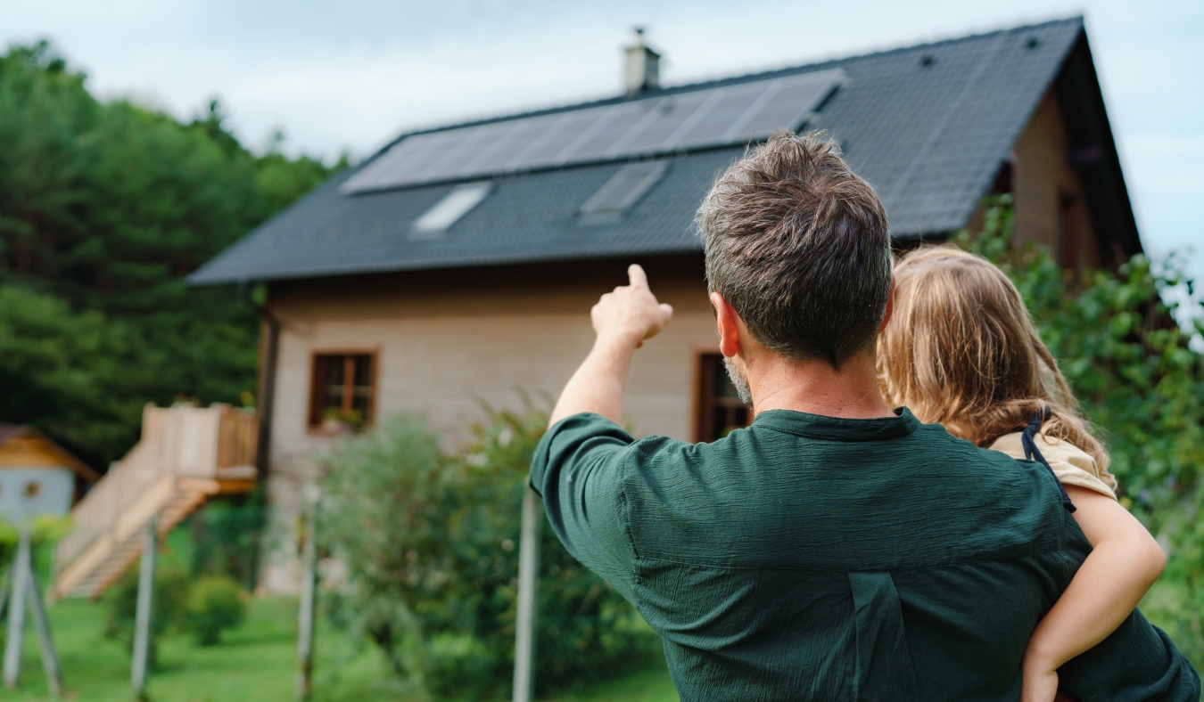 Rear view of dad holding her little girl in arms and showing at their house