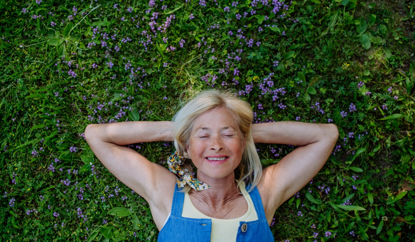 relaxed senior woman lying down in field of wild thymus flowers