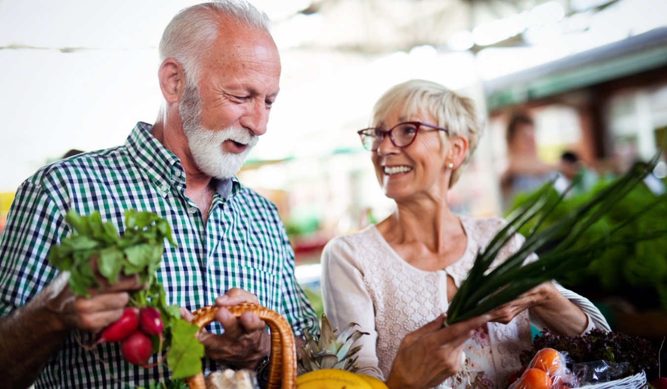 Smiling senior couple holding basket with vegetables at the market