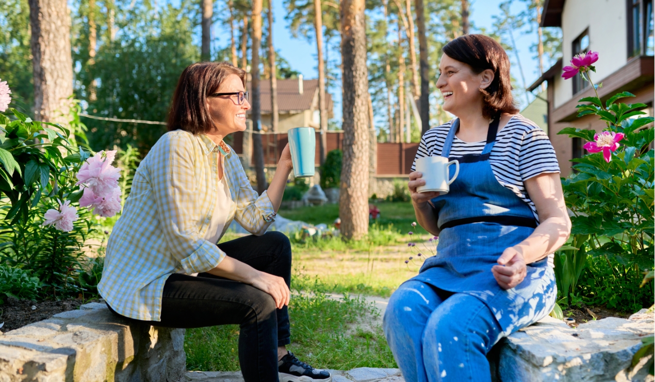 two middle aged woman enjoying coffee tea in garden