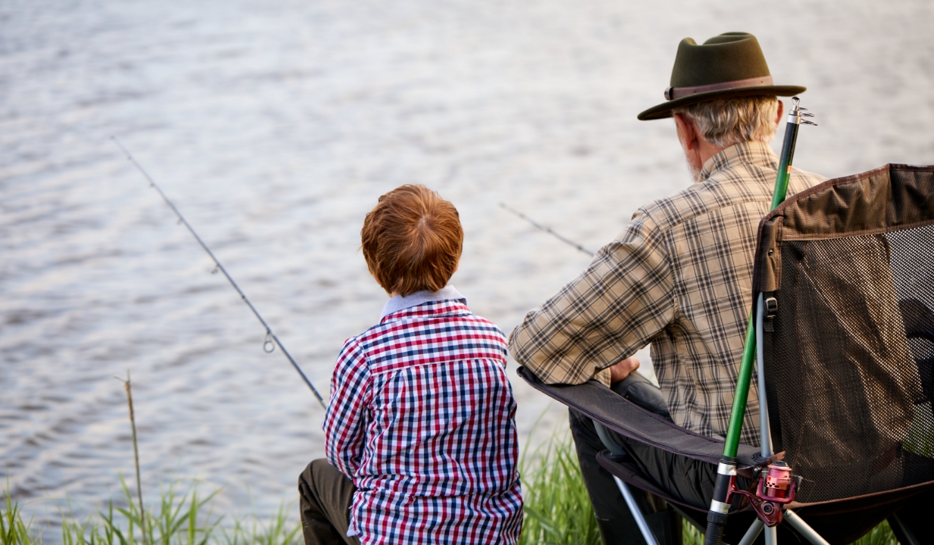 grandfather and boy fishing by lake together during camping