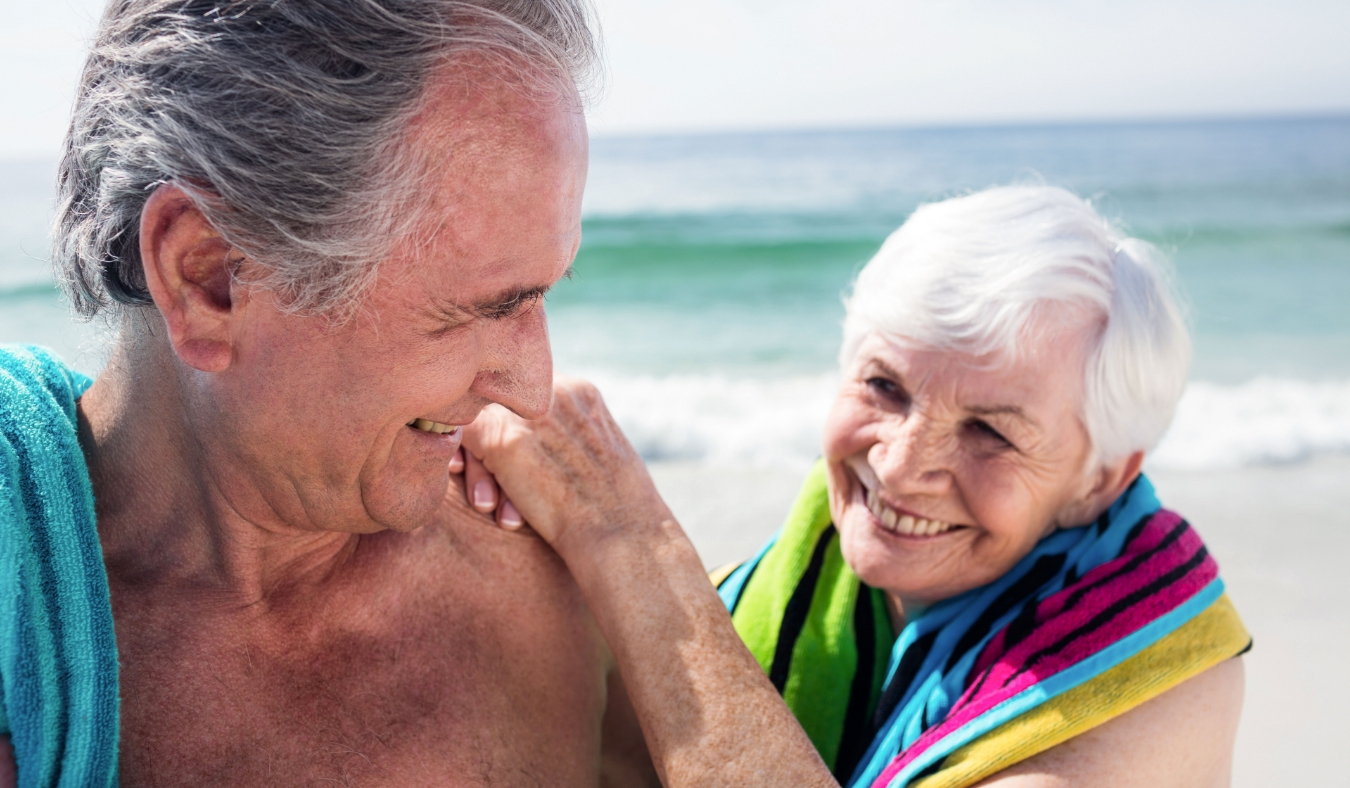 Happy senior couple holding a towel around neck on beach