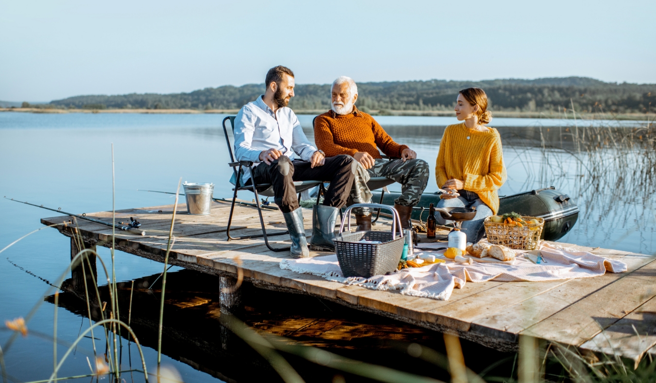 Man and woman with senior grandfather having a picnic with vegetables and fresh caught fish
