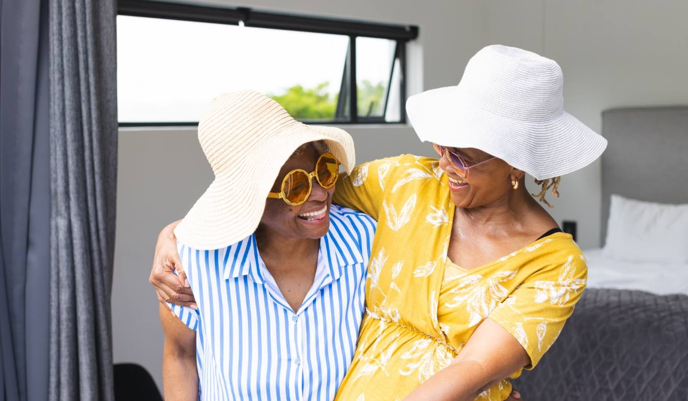 Senior African American woman and biracial woman wear stylish sunhats and sunglasses on vacation