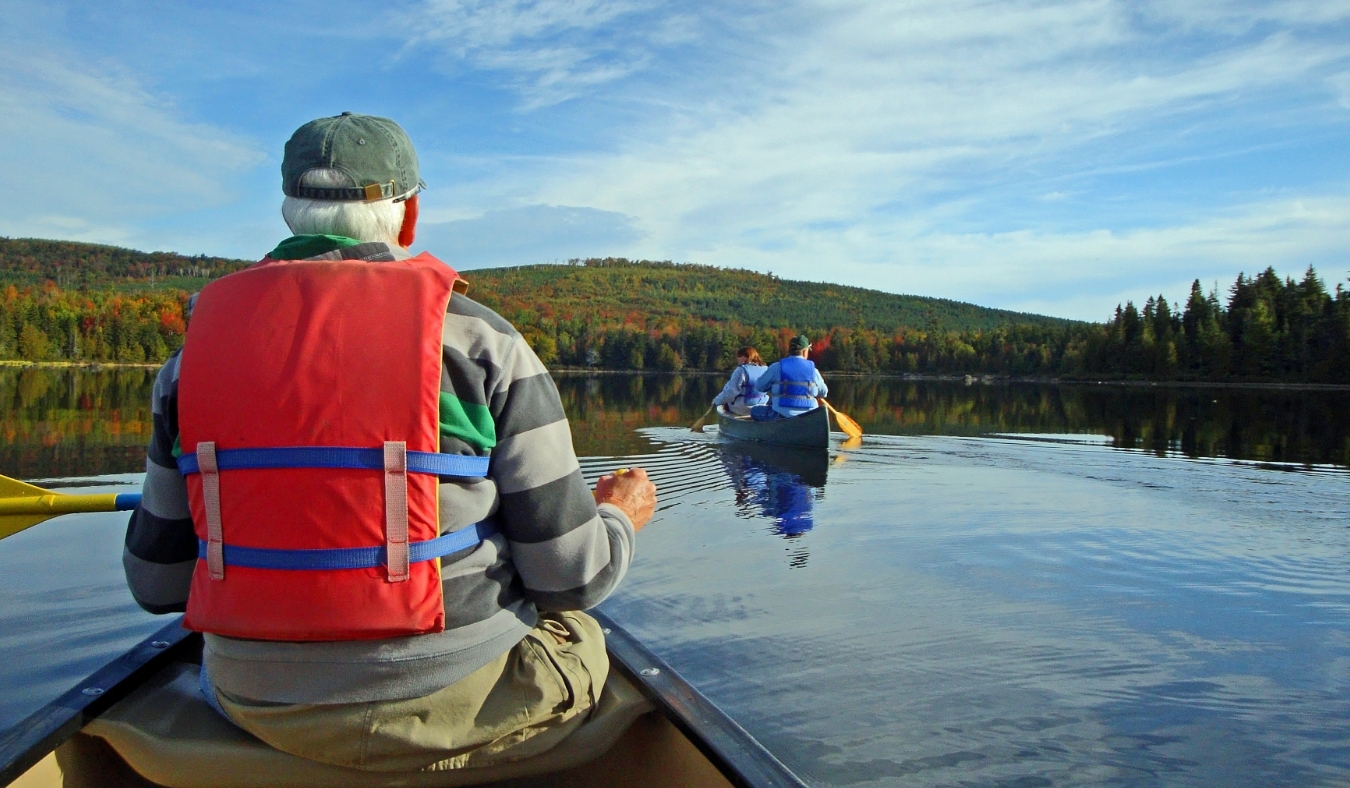 Senior man paddling a canoe with second canoe