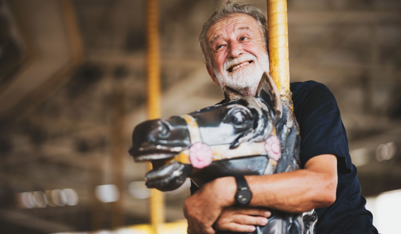 senior man riding merry go round at amusement park