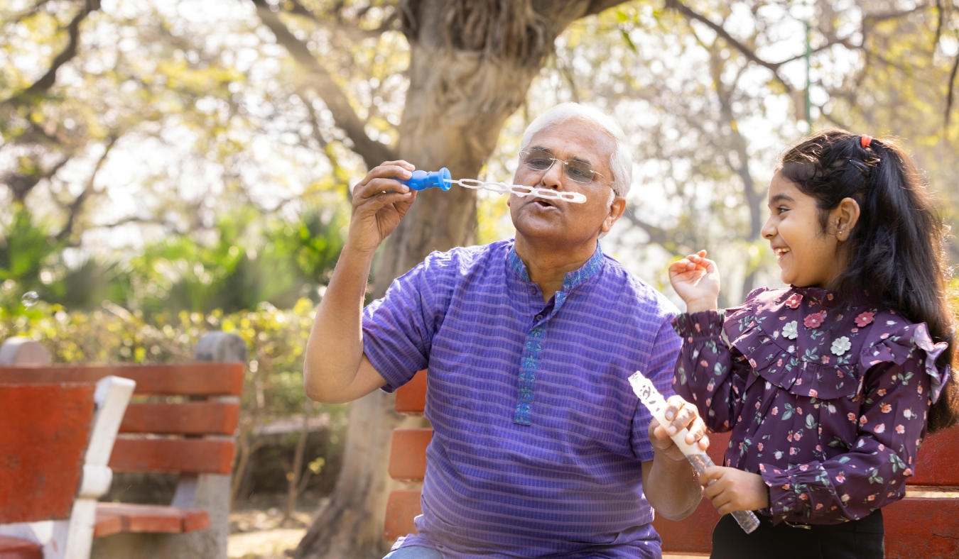 Senior man with granddaughter having fun blowing bubbles at park
