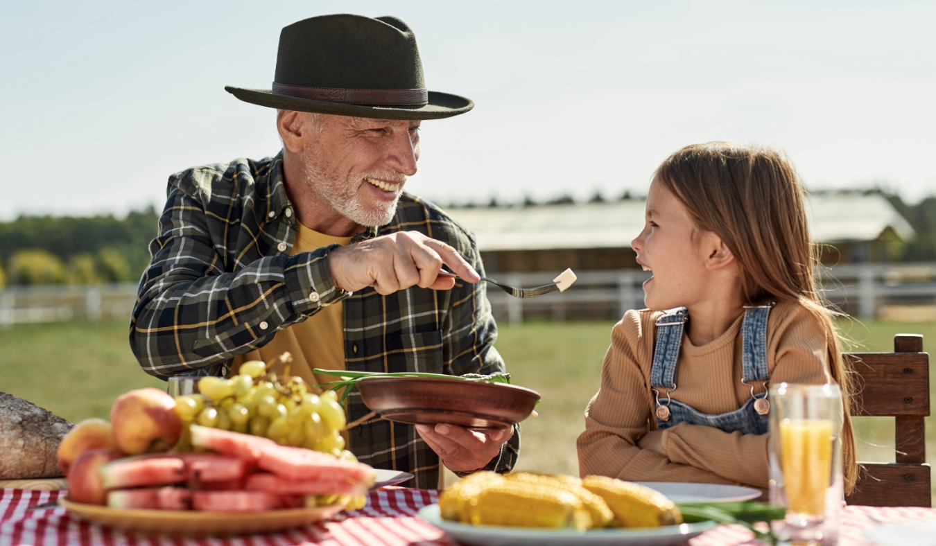 Smiling grey hair grandfather feeding cheese his little granddaughter