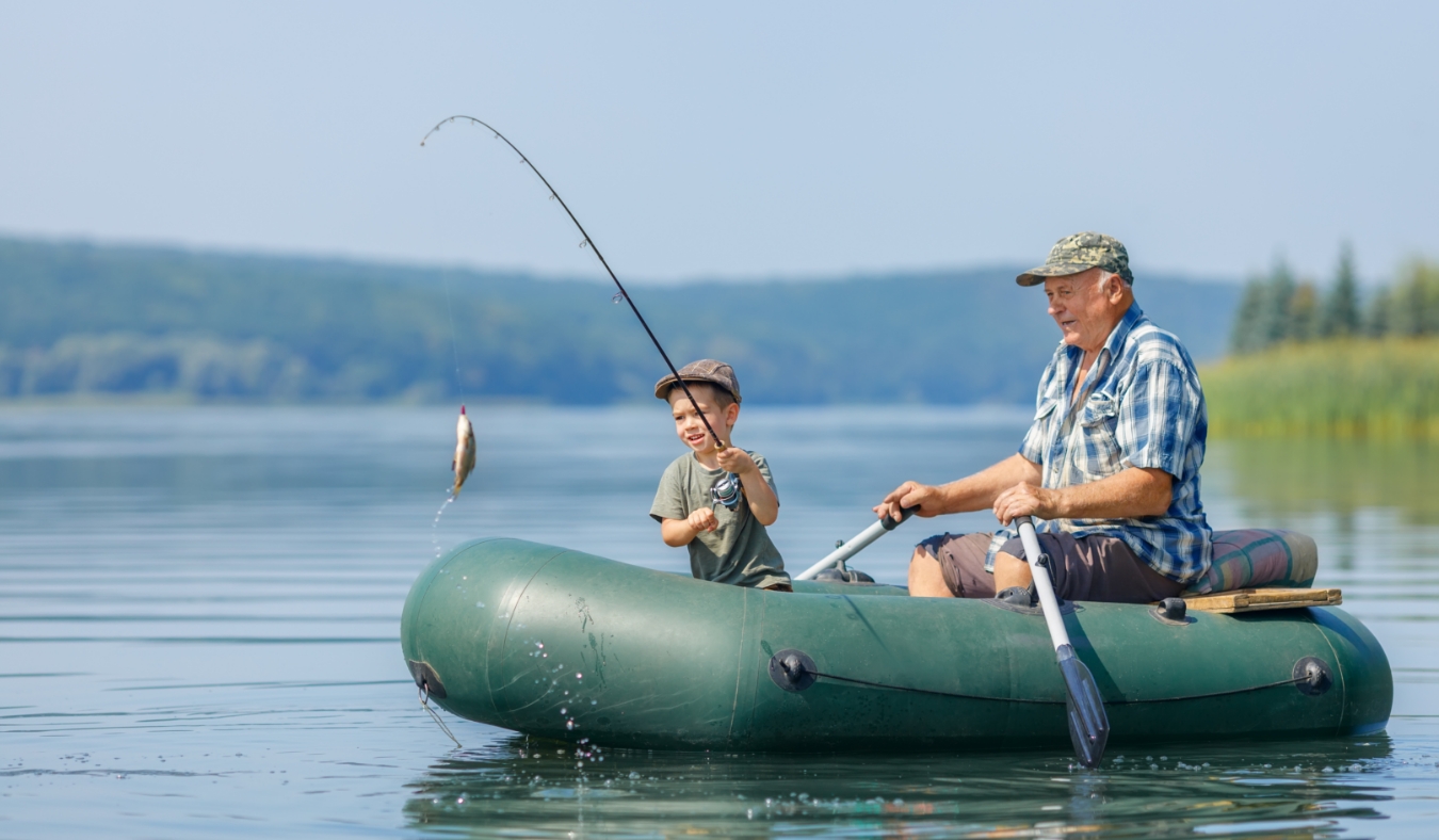 smiling little boy with elderly grandfather together fishing on the river