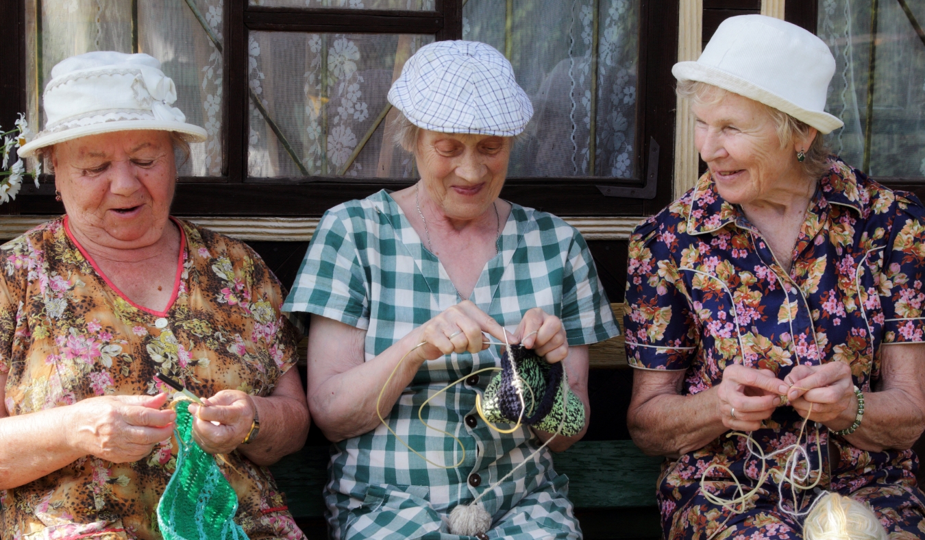 three senior friends knitting on a bench together