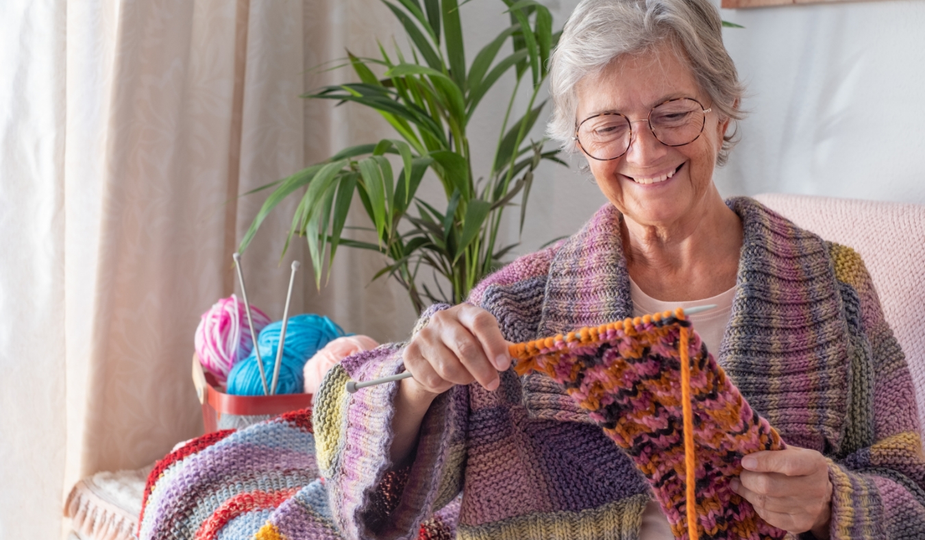 senior smiling woman sitting on sofa at home while knitting