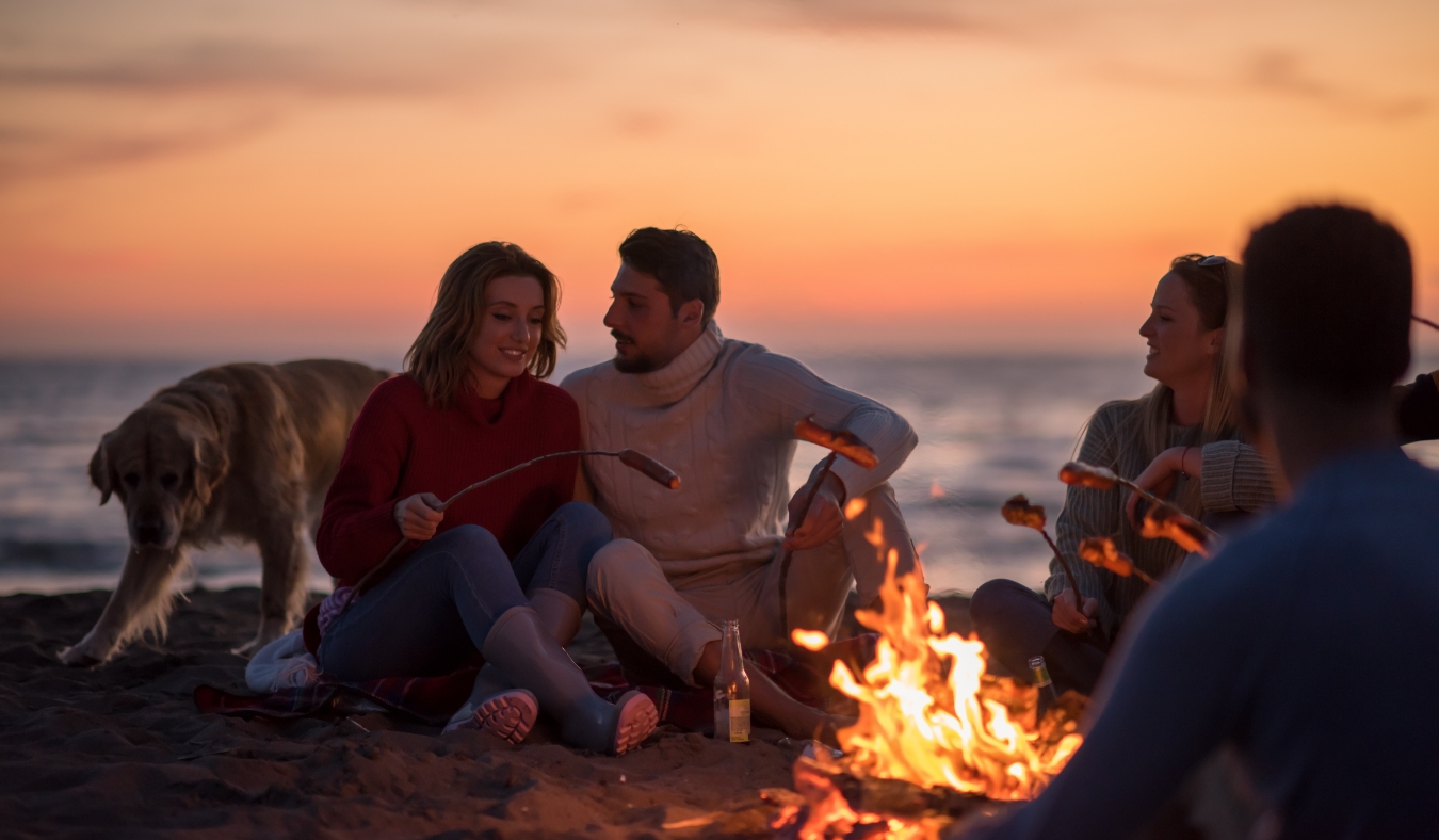 young friends sitting by the fire at autumn beach