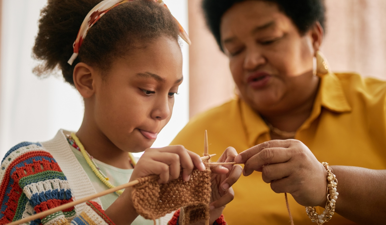 african american young girl learning knitting while grandmother