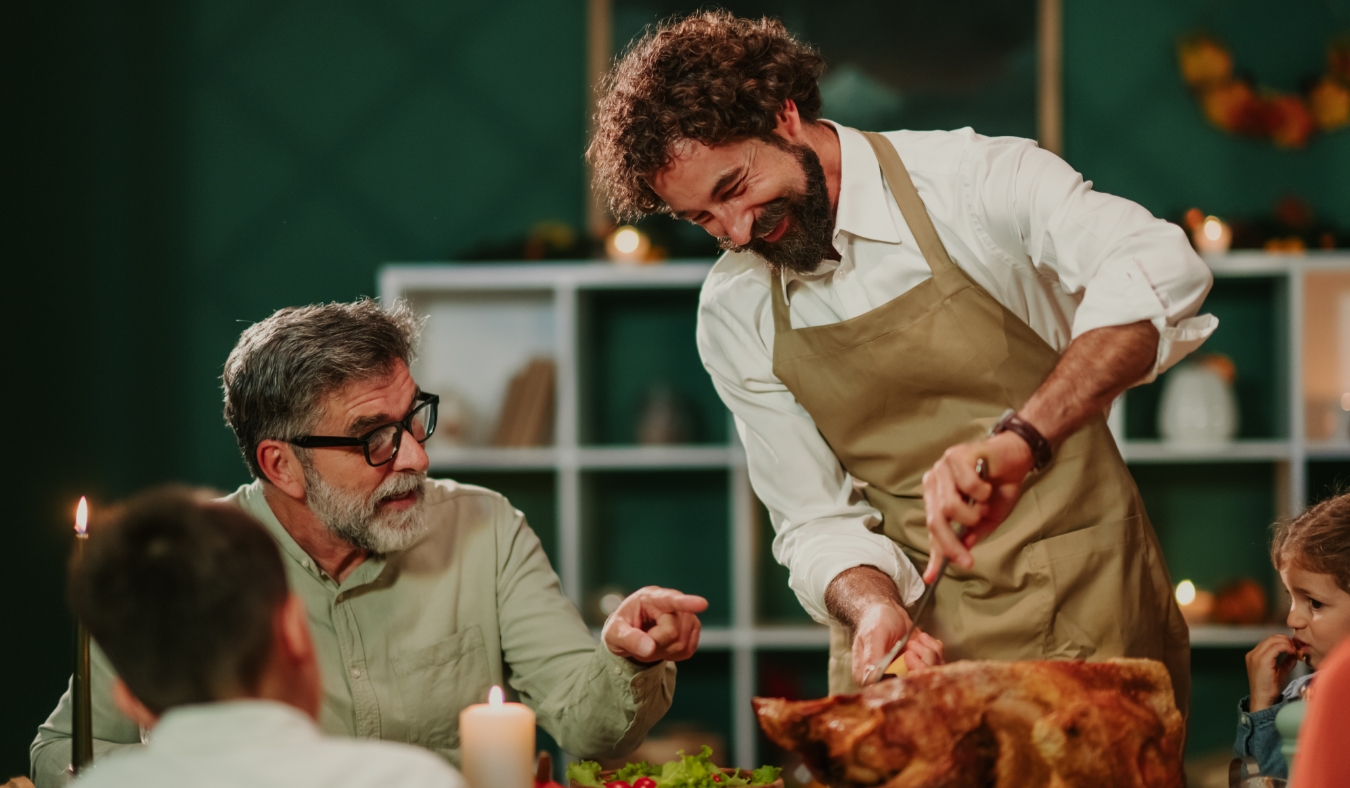 grandfather instructing adult son how to cut turkey for dinner