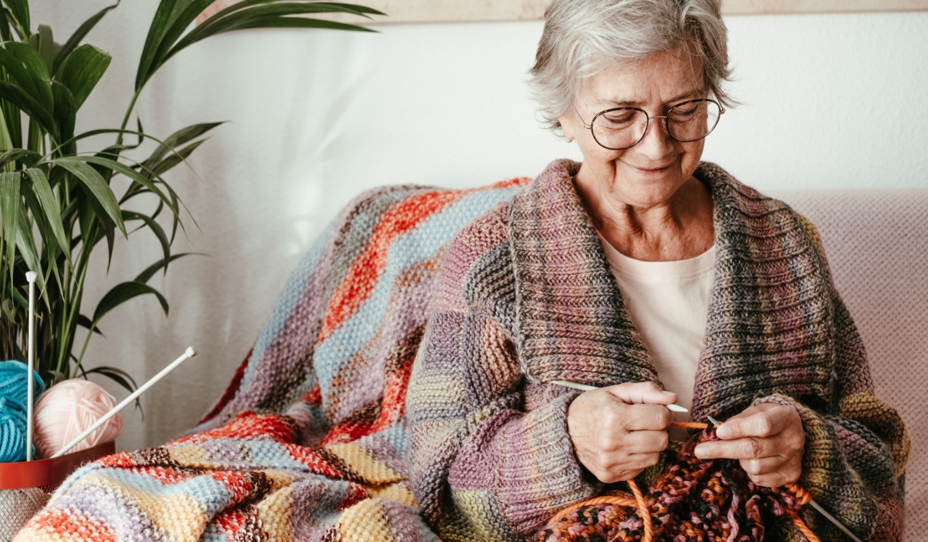 mature woman sitting on sofa at home while knitting