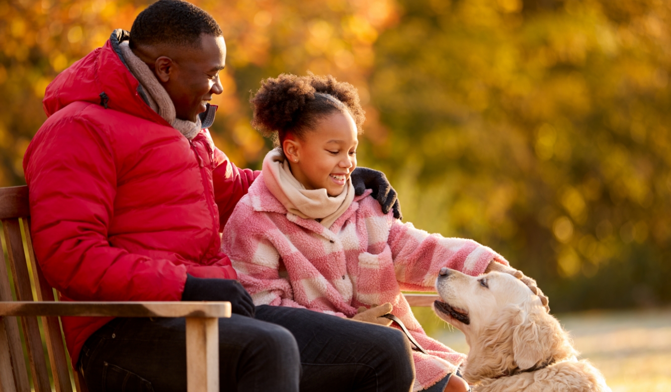 father daughter smiling with dog on park bench