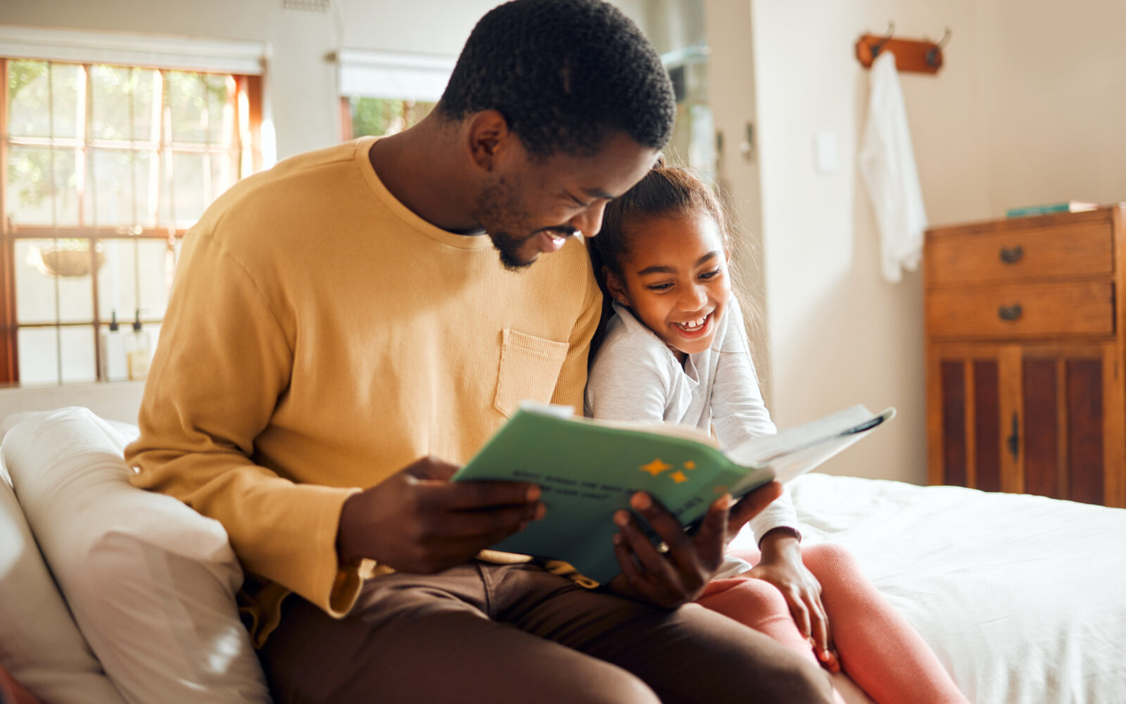 African American adult male reading to an African American female child.